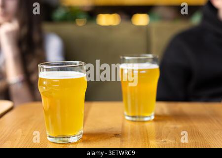 Zwei Gläser trübes Bier auf Holztisch. Zwei Gläser goldbraunes Bier mit schaumigen Tops sitzen auf einem Holztisch in einer sanft verschwommenen Bar-Umgebung mit Stockfoto