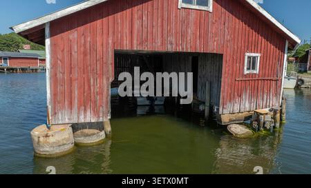 Aus der Vogelperspektive eines roten hölzernen Bootshauses in Rosala, mit verwitterten Holzwänden und einem kleinen Boot, das im Inneren über dem ruhigen Wasser Kimitoon, Südwesten F, verankert ist Stockfoto