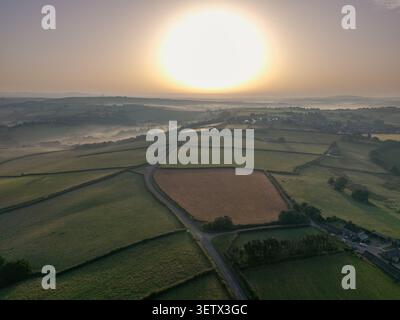 Aus der Vogelperspektive sehen Sie den Sonnenaufgang über grünen Feldern und nebeligen Tälern rund um das Dorf Lanreath in Cornwall, England Stockfoto
