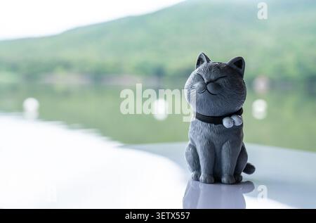 Chiang Mai, Thailand - 22. Juni 2026 : dunkelgraue Katzenfigur mit schwarzem Kragen auf reflektierender Oberfläche mit lächelndem Ausdruck und Reservoir mou Stockfoto