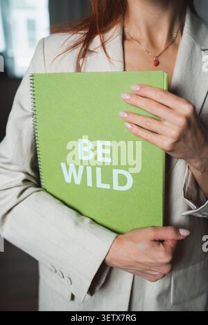 Frau hält grünes Notizbuch mit klarem Text auf dem Einband in einer Innenumgebung am Tag Stockfoto