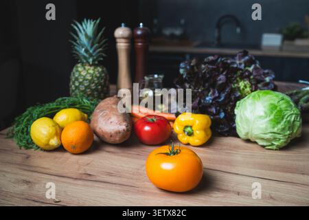 Frische Früchte und Gemüse, die tagsüber auf einem Holztisch in einer Küche ausgebreitet sind Stockfoto