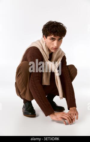 Ein hübscher junger Mann in schicker Kleidung posiert elegant im Hocken und zeigt seinen Stil. Stockfoto
