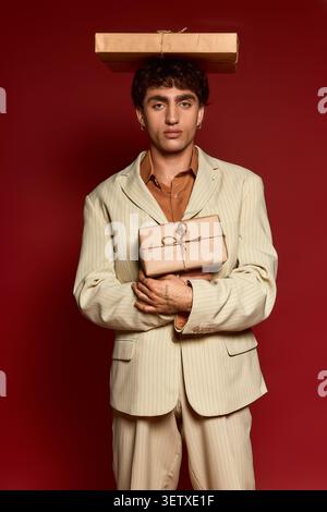Ein hübscher junger Mann steht elegant gekleidet in einem stilvollen Anzug und balanciert Geschenke auf seinem Kopf. Stockfoto