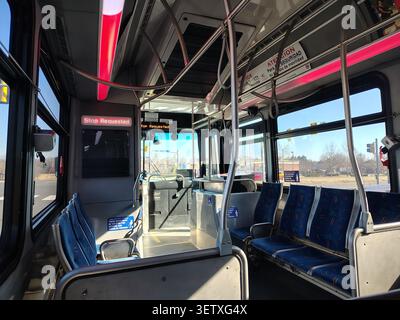 Reihen blauer Stoffsitze mit Hinweisschildern in einem verlassenen Bus. Die Straße ist durch die großen Seitenfenster und die Windschutzscheibe sichtbar Stockfoto