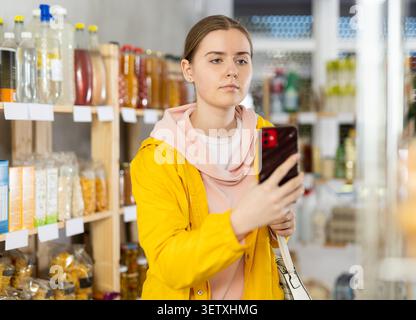 Mädchen scannt QR-Code auf Produkten in Supermarktregalen, um das Ablaufdatum zu überprüfen Stockfoto
