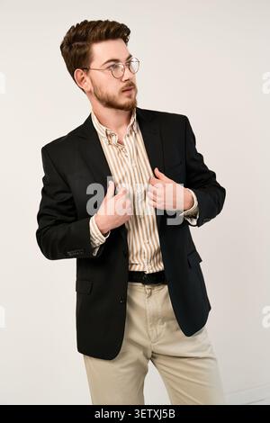 Ein bärtiger junger Mann posiert selbstbewusst in seinem stilvollen und eleganten Outfit Stockfoto