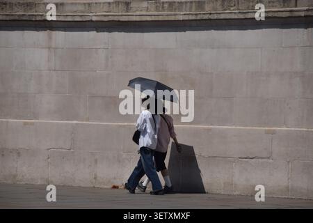 London, UK, 24. Juni 2026. Frauen schützen sich unter einem Schirm vor der sengenden Sonne am Trafalgar Square, während das Met Office eine gelbe Warnung vor extremer Hitze ausgibt. Quelle: Vuk Valcic/Alamy Live News Stockfoto