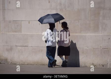 London, UK, 24. Juni 2026. Frauen schützen sich unter einem Schirm vor der sengenden Sonne am Trafalgar Square, während das Met Office eine gelbe Warnung vor extremer Hitze ausgibt. Quelle: Vuk Valcic/Alamy Live News Stockfoto