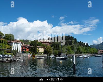 Malerische Uferszene von Bellagio mit verankerten Segelbooten, farbenfrohen Häusern am See und grünen, mit Zypressen bedeckten Hügeln. Stockfoto