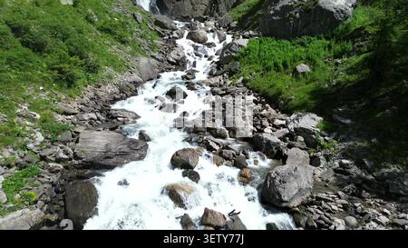 Aus der Vogelperspektive auf einen rauschenden Bergbach, der über Felsen mit üppig grünen Hängen in der Nähe des Lac de Tseuzier in Crans-Montana, Wallis, Schweiz, kaskadiert Stockfoto