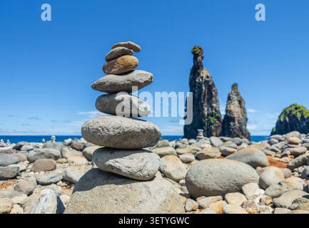 Ein ausgeglichener Zen-Steinstapel auf einem Kiesstrand mit majestätischen vulkanischen Meeresfelsen im Hintergrund, Madeira, Strand von Ribeira da Janela, Portugal Stockfoto