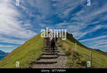 Eine Gruppe von Wanderern klettert die Steinstufen des Stoos Ridge Trail zu einem sonnendurchfluteten Kamm Stockfoto