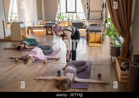 Lehrerin, die Mobilität einer Gruppe von Senioren in einem Pilates-Studio beibringt. Gruppe von Senioren, die auf Matten trainieren, um das Gleichgewicht zu verbessern und Stockfoto