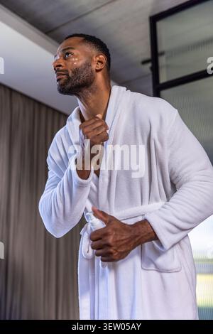 Reifer afroamerikanischer Mann, der Deodorant im Badezimmer aufträgt, trägt weißen Frotteeband Stockfoto