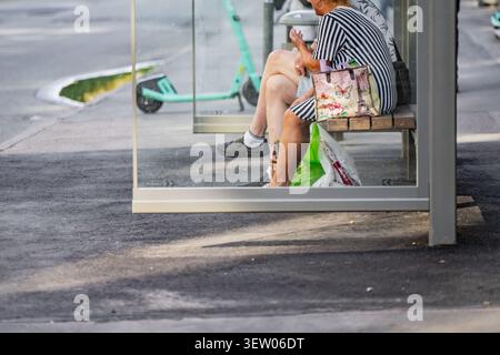 Offener Schuss von älteren Passagieren, die in einer Glasbushaltestelle sitzen und auf den Transit warten, der den öffentlichen Nahverkehr repräsentiert Stockfoto