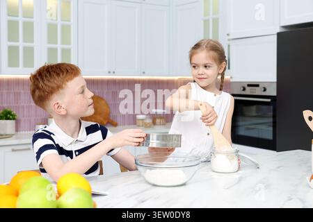 Bruder und Schwester machen Teig am weißen Marmortisch in der Küche Stockfoto