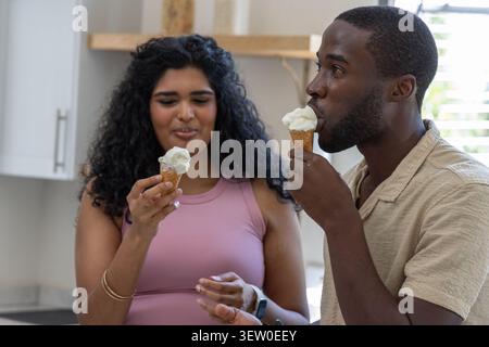 Diverse Paare in der Küche, die Waffelkegel mit Vanillekugeln halten, Mann bringt Kegel zum Mund Stockfoto