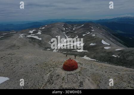 Blick aus der Vogelperspektive auf Bivacco Cesare Mario Pelino auf dem felsigen Bergrücken mit Schneeflocken und zwei Wanderern in der Nähe von Fara San Martino, Abruzz Stockfoto
