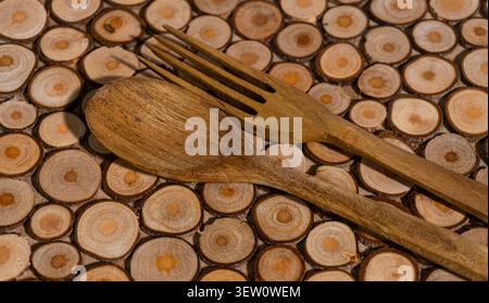 Nahaufnahme von Vintage-Holzlöffel und -Gabel, die auf einer Oberfläche aus angeordneten kleinen Holzzweigen aufliegen und Texturen aus altem Holz zeigen Stockfoto