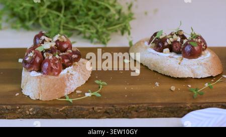Zwei Scheiben knuspriges Baguette mit Ziegenkäse, gerösteten Trauben und gehackten Walnüssen. Mit frischen Thymianzweigen, diese Vorspeisen Stockfoto