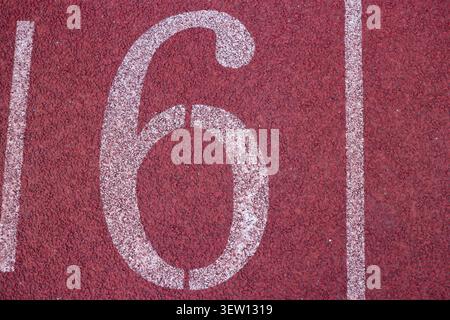 Flacher Lay-Shot einer großen weißen Nummer 6, die auf einer roten gummierten Laufbahn in einem Sportstadion im Freien gemalt ist. Stockfoto