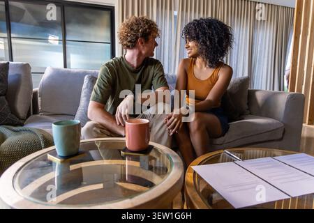 Verschiedene Paare sitzen auf dem Sofa im Wohnzimmer und machen Augenkontakt neben Kaffeetischen mit Tassen Stockfoto