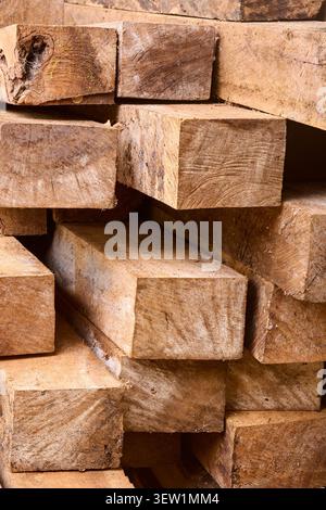 Gestapelte quadratische Holzbalken in Nahaufnahme, rohes braunes Holz mit rauer Körnung und Sägemarkierungen, Vollrahmen-Hintergrundstruktur der Baumaterialien Stockfoto