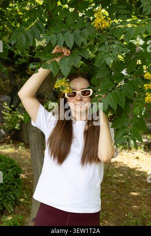 Eine junge Frau, die draußen eine stilvolle Sonnenbrille mit Wildblumen im Haar trägt Stockfoto