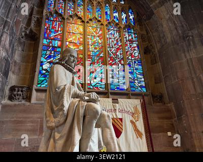 Die Steinstatue von Humphrey Chetham aus dem Jahr 1853 steht vor dem lebendigen Buntglasfenster in der Kathedrale von Manchester, England. Stockfoto