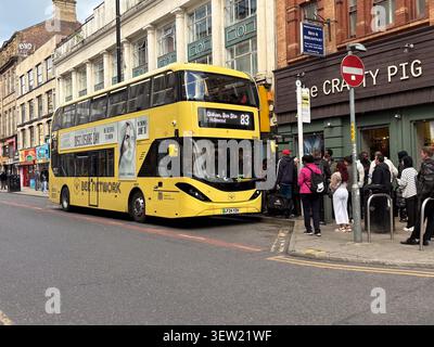 Pendler steigen an einer Straßenhaltestelle in Manchester in einen hellgelben Doppeldeckerbus von Bee Network ein. Stockfoto