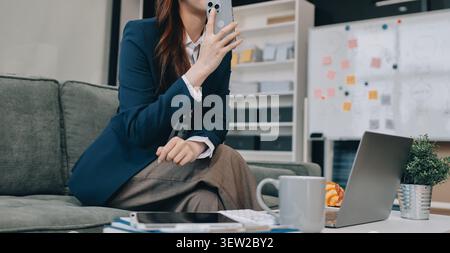Junge asiatische Geschäftsfrau, die am Telefon telefoniert und bei der Arbeit ein digitales Tablet verwendet Stockfoto