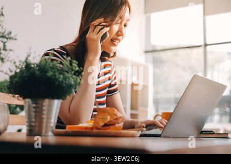 Glück Unternehmer schönes Geschäft asiatische junge Frau tragen lässig Handy zum Einkaufen online genießen Sie mit sozialen Medien und Laptop zu Hause Stockfoto