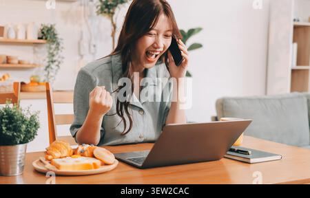 Glück Unternehmer schönes Geschäft asiatische junge Frau tragen lässig Handy zum Einkaufen online genießen Sie mit sozialen Medien und Laptop zu Hause Stockfoto