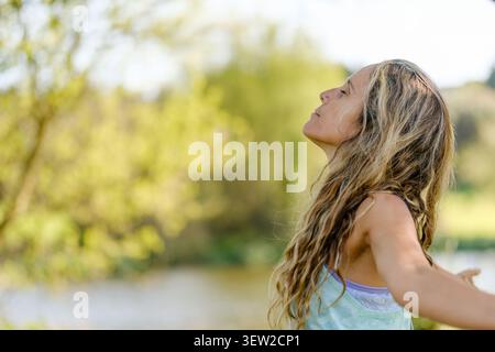 Frau steht draußen, Arme offen, atmet frische Luft und fühlt sich ruhig Stockfoto