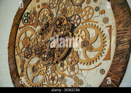 Dieses schöne Innenraumfoto zeigt eine große dekorative Steampunk-Wanduhr aus natürlichem Holz, die aus einem kreativen Dreiviertelwinkel aufgenommen wurde. Die Stockfoto