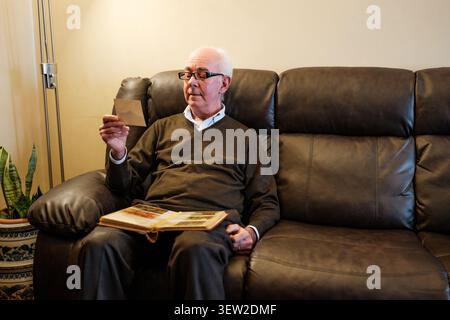 Ein älterer Mann erinnert sich an alte leere Fotos und das Album auf dem Sofa Stockfoto