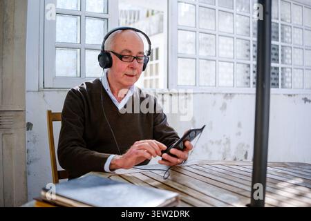 Seniorenmann, der sich im Freien entspannt und Musik auf seinem Smartphone mit Kopfhörern hört Stockfoto