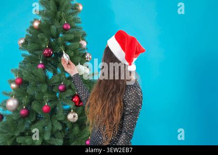 Frau, die sorgfältig eine schöne Dekoration an einem festlichen grünen Weihnachtsbaum hängt Stockfoto