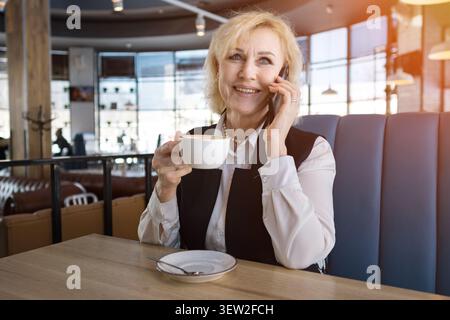 Ältere Kaukasische Frau Genießt Kaffee Und Unterhaltung. Reifer Geschäftsmann, Der Sich An Einem Freundlichen Telefongespräch Beteiligt. Ältere Kaukasische Frau Bei Stockfoto