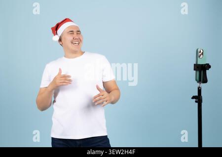 Ein Mann, der einen Weihnachtsmütze trägt und lächelt, während er vor einem Mikrofon steht Stockfoto
