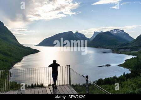 Mann, der mit dem Rücken zur Kamera auf der Bergsbotn-Plattform steht und auf die Berge und den Fjord der Insel Senja blickt Stockfoto