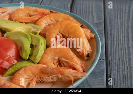 Gekochte Garnelen mit frischer Avocado und Tomate auf Teller über blauem Holztisch Stockfoto