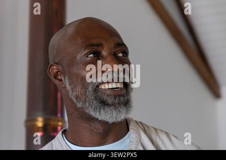 Ranghoher Afroamerikaner lächelnd, sah im Zimmer links und trug ein blaues Hemd in der Nähe von Metallrohren Stockfoto