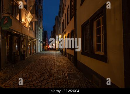 Nachtansicht der historischen Kopfsteinpflastergasse Lintgasse, beleuchtet von Straßenlaternen in der Altstadt von Köln, Deutschland. Stockfoto