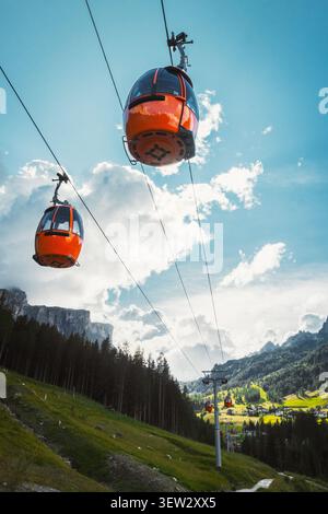 Dolomiten, Italien - 27. juli 2026: Gondelbahn Colfosco Orange über saftig grüne Almwiesen Wanderweg Tal Stadt Kiefernwald towe Stockfoto