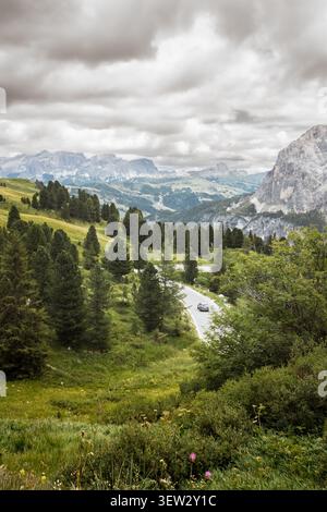 Ein Auto aus der Vogelperspektive fährt eine gewundene Bergstraße durch die Dolomiten-Landschaft mit Alpenwald, rustikalen Hütten, grünen Wiesen und Dramatten Stockfoto