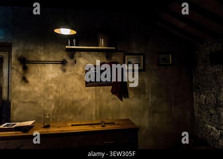 Innenansicht eines schwach beleuchteten historischen Raums mit einem Holztisch, hängenden Lampen und einer Tafel, auf der beschlagnahmte illegale Schnapsfässer beim Jameson D verzeichnet sind Stockfoto