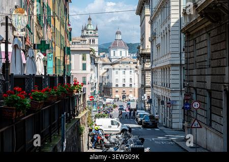 Blick eine schmale Stadtstraße hinunter, die mit historischen mehrstöckigen Gebäuden gesäumt ist und an einem sonnigen Tag in Genua, Italien, auf eine markante Kuppelkirche zuführt Stockfoto
