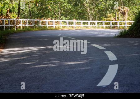 Kurvige Asphaltstraßenkurve mit White Divider Line und Leitplanke Ein Low-Winkels-Bild unterstreicht die Struktur einer leeren Asphaltstraße, während sie scharf kurvt Stockfoto